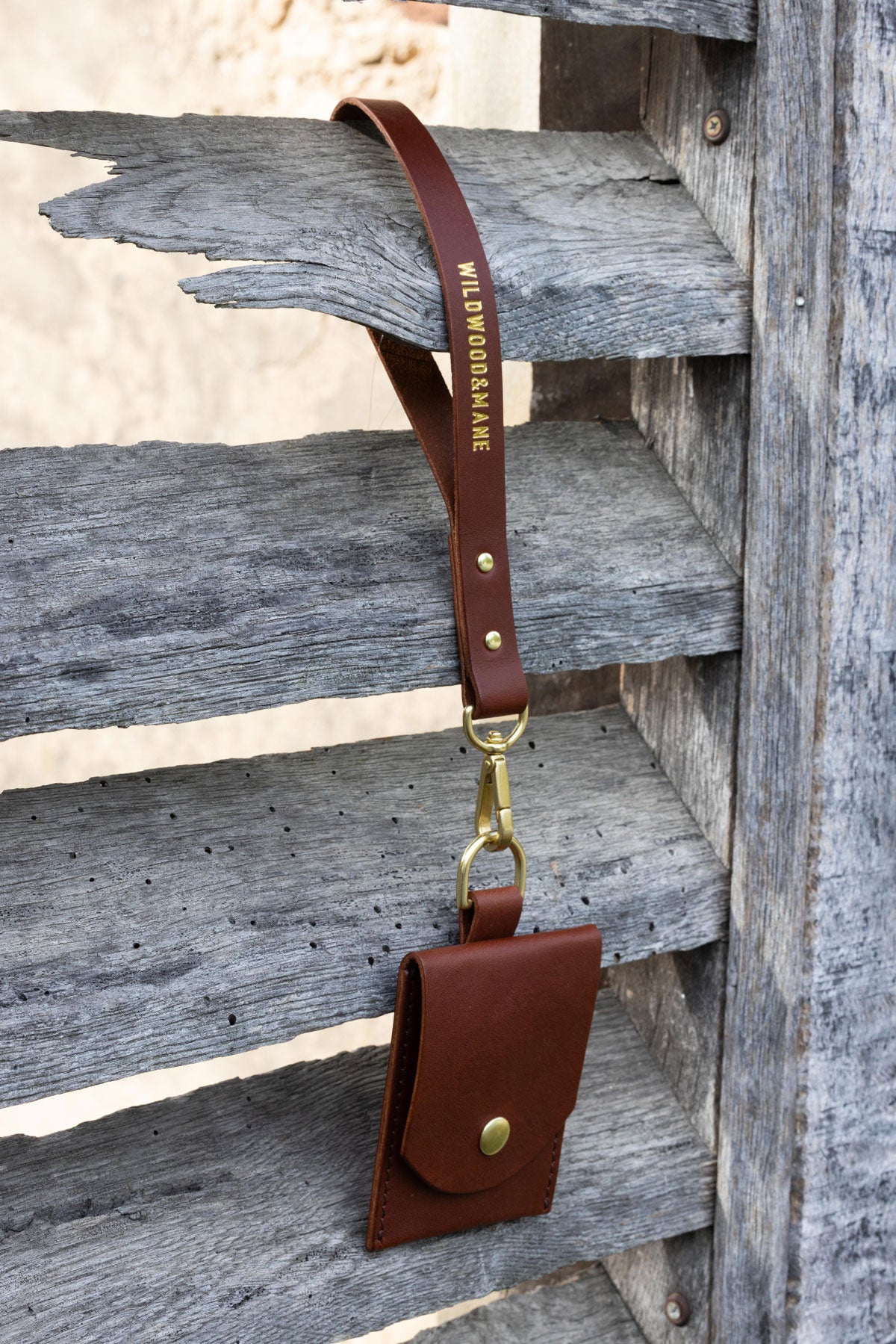 Brown leather wallet with wrist strap on a wooden shutters. Front View
