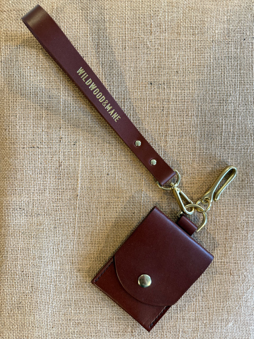 Brown leather wallet with wrist strap on a beige burlap background with fish hook key chain